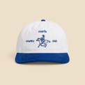 White and Liberty-blue Marfa Country Club Rider’s Cap on a clean warm beige background